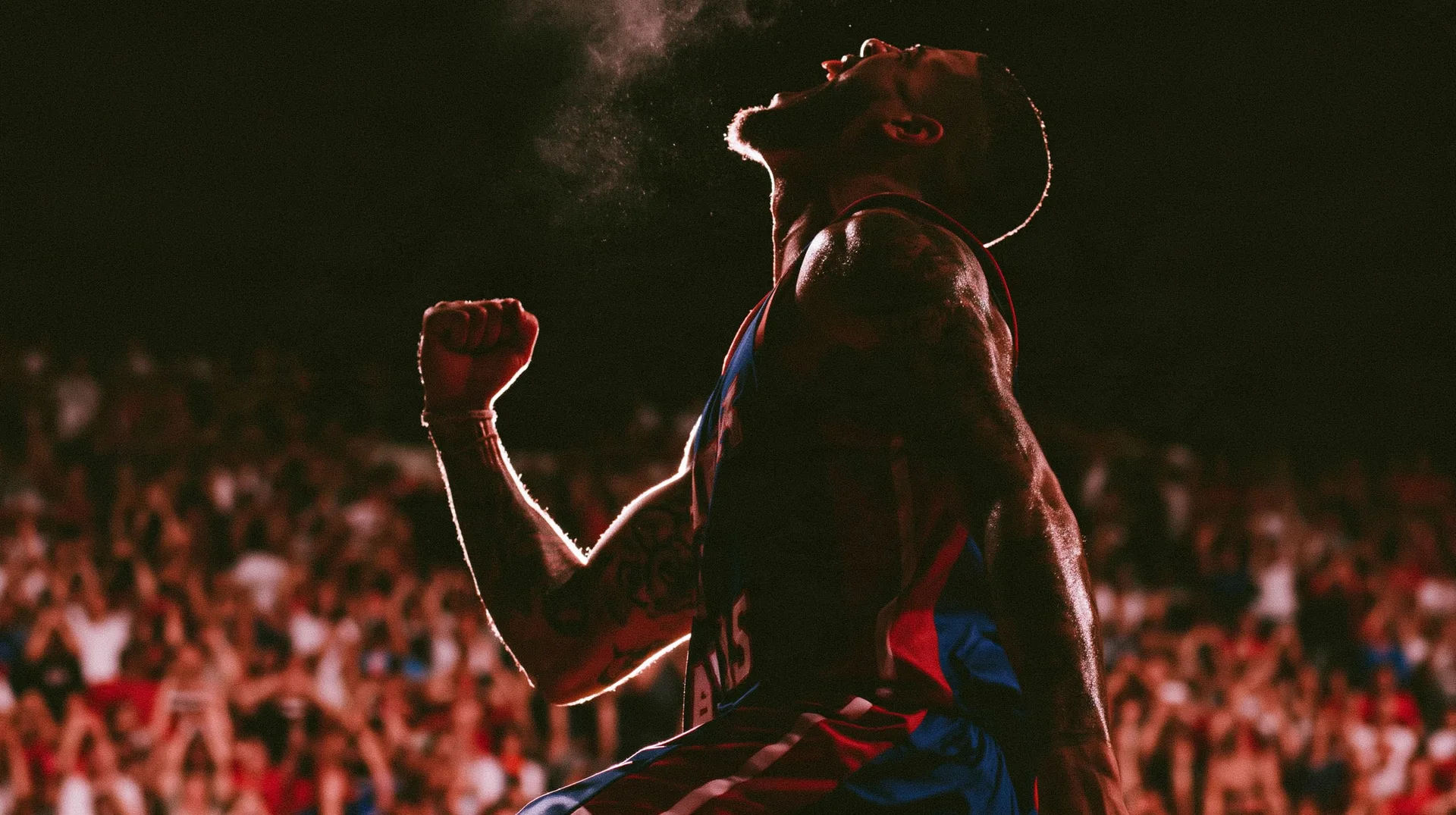 An NBA player roaring in celebration before a packed arena crowd at night.